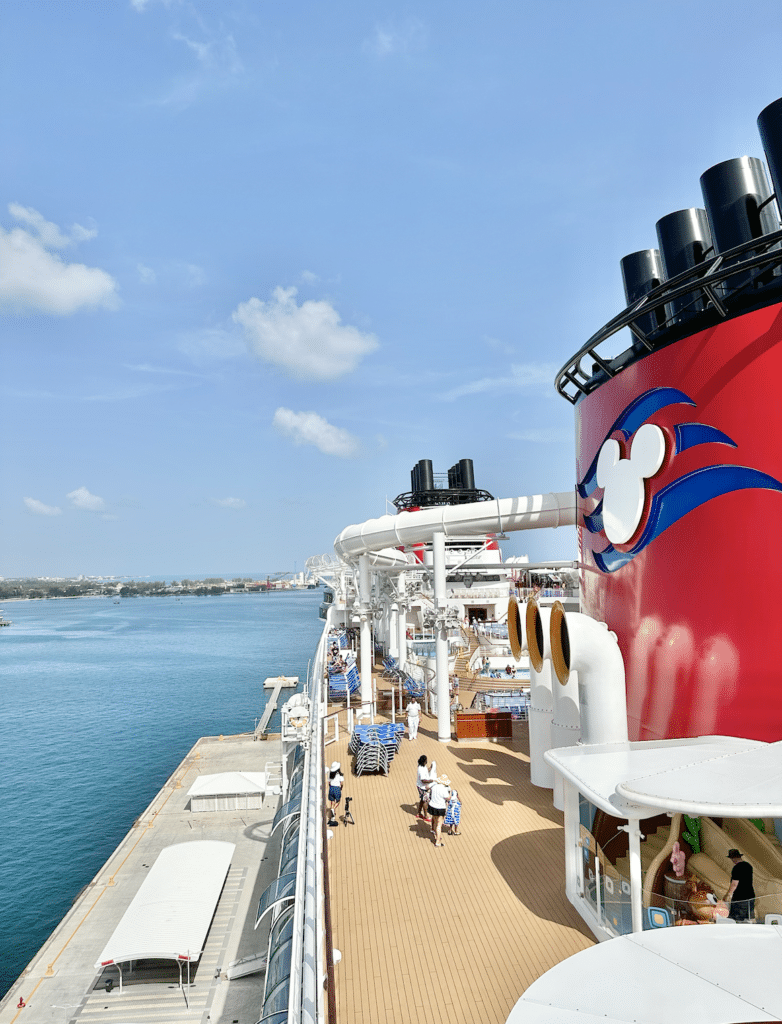 Disney Cruise ship deck with Mickey-shaped smokestack, docked at port on a sunny day.